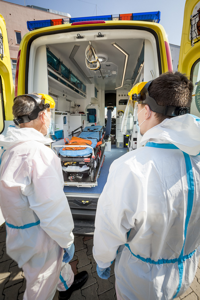 Dwóch ratoników medycznych stoi tyłem przy otwartych drzwiach ambulansu 