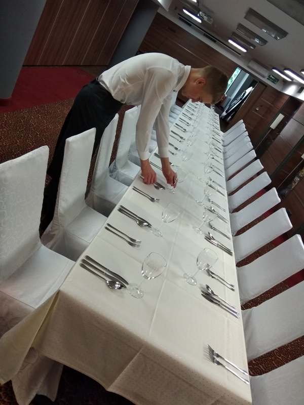 Uczeń nakrywa stół podczas praktyk w hotelowej restauracji