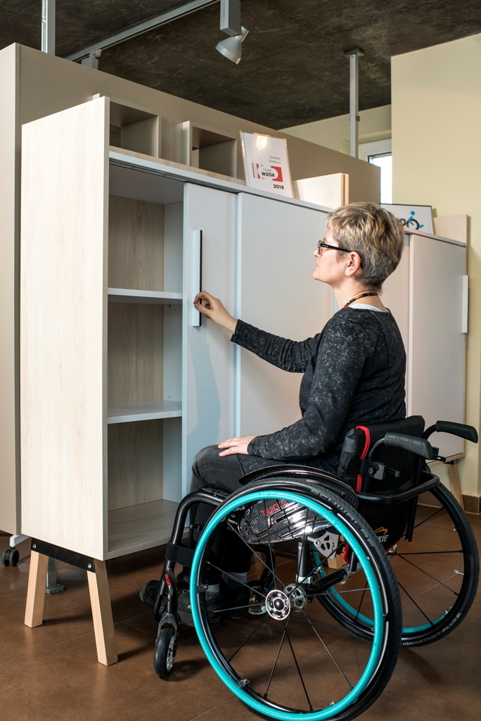 Kobieta na wózku otwiera szafę / A woman on the wheelchair is opening an office locker 